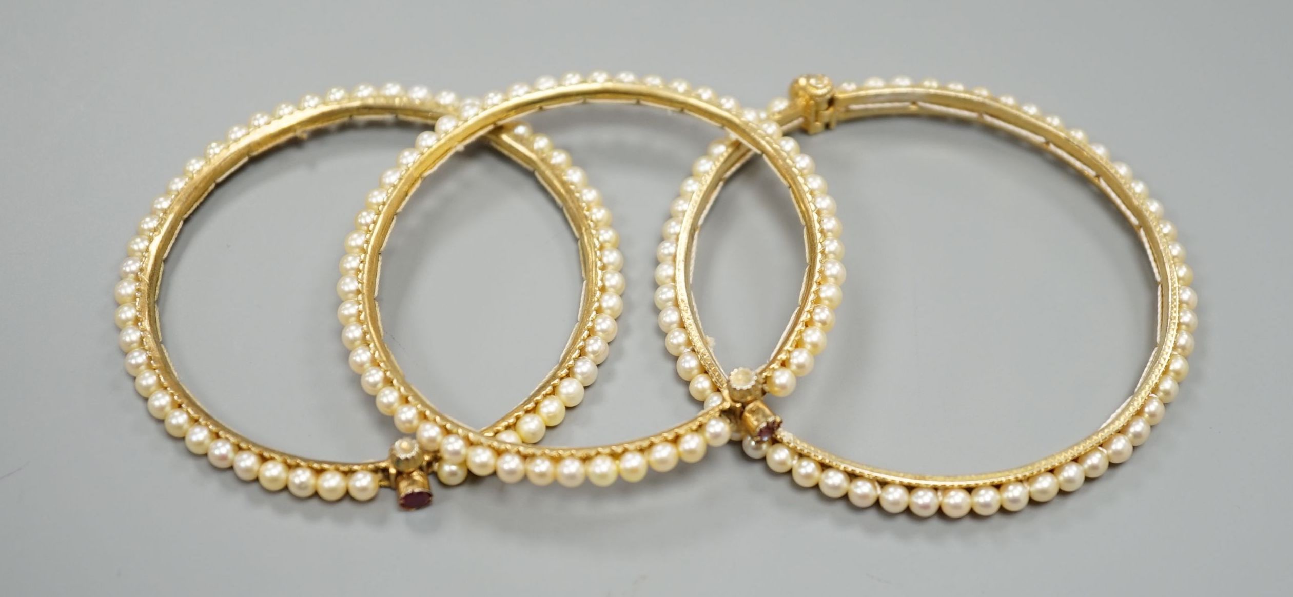 Three gilt white metal and cultured pearl set bangles.